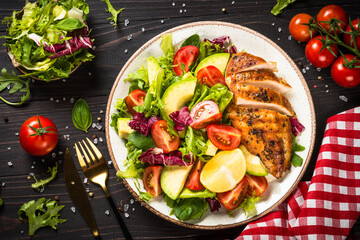 Healthy food concept. Grilled chicken with fresh salad. Top view at dark wooden table.