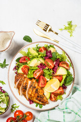 Healthy salad with Grilled chicken fillet, fresh leaves, avocado and vegetables. Top view at white marble table.