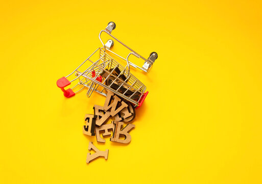 scattered wooden letters of the English alphabet from a miniature shopping trolley on a yellow background, close-up. Copywriting and education concept. Copy space. - Powered by Adobe