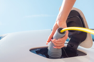 Female hand, opening a socket cover and plugging in the charger in an electric car at a charging...