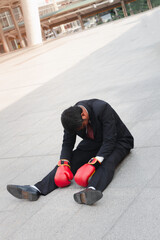 Business concept : Businessman wearing red boxing gloves sits on the floor, he was stressed about financial problems. The bad economic conditions caused the company to lose.