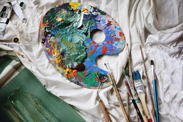 Artist paint brushes and palette on white cloth background.