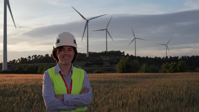 Successful woman wearing safety helmet and working in wind farm smiling and looking at camera.