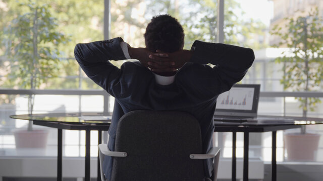 Rear view of afro-american businessman working at desk and stretching in office - Powered by Adobe
