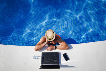 bird view of remote online working digital nomad man on workation with hat &  laptop at a white...