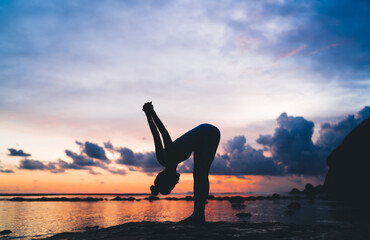 Side silhouette view of slim woman have productive stretching workout during sunset time at seashore, flexible female keeping healthy lifestyle enjoying warm up pilates exercising at coastline