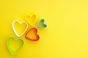 Plastic molds of multi colors for making cookies in the shape of a hearts on a yellow background.