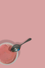 Cover page with a fruits yogurt in a plastic packaging and a teaspoon at solid pink background with copy space. Concept of healthy food, vitamins and healthy life.