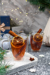 Christmas card. Two glass cups of tea with lemon and cinnamon sticks close-up on a Christmas background. Warm medicinal winter tea in glass cups on the background of a pine branch.