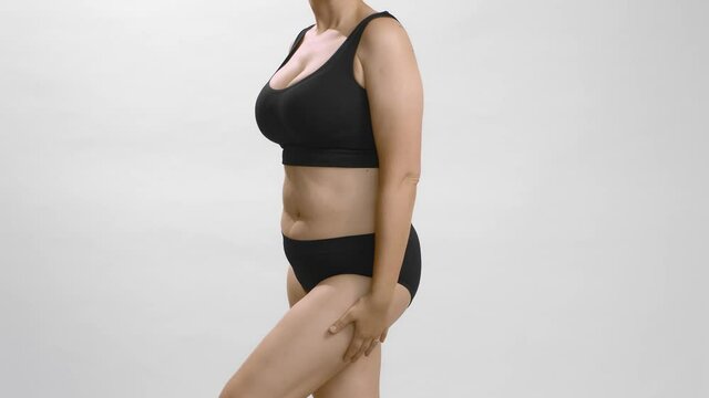 Full figure caucasian woman in black bra and briefs is touching, embracing and moving to show each side of her body with hands on the waist. Studio still medium shot no face video.