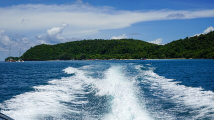 The ship was sailing in the middle of the sea with the deep blue sea, the mountains and the clear sky.