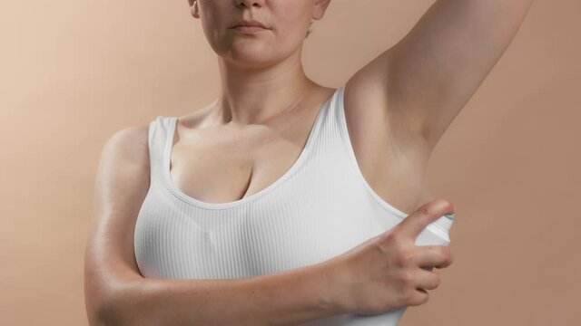 White young lady lift the hand and use antiperspirant to avoid stinking and bad smell. Clean seamless white bra. Studio slow motion video on beige background.