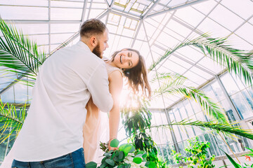 Portrait of a groom in a wedding suit and a bride in a dress having fun in a green botanical garden full of greenery
