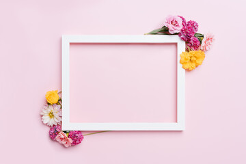 Wooden frame decorated with flowers on a pink pastel background. Top view mockup with copy space.