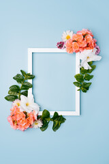 Wooden frame decorated with flowers on a blue pastel background. Top view mockup with copy space.