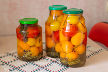 Canned food is different. Various glass jars with red and yellow tomatoes on the table.