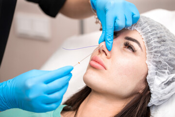 Cosmetic procedure for non-surgical rhinoplasty. The beautician inserts cosmetic threads into the...