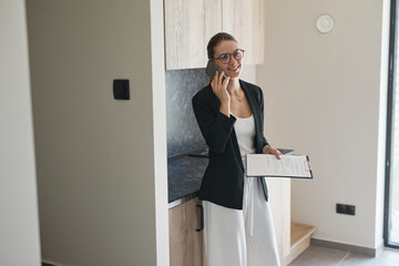 Portrait of female real estate agent speaking by smartphone indoors in house for sale, copy space