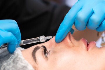 Cosmetic procedure for non-surgical rhinoplasty. The beautician inserts cosmetic threads into the...