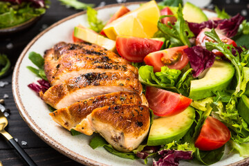 Healthy food concept. Grilled chicken with fresh salad at dark wooden table.