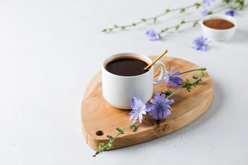 Chicory drink in a white mug with chicory flowers next to it on a wooden board. - obrazy, fototapety, plakaty