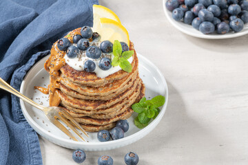 Healthy summer breakfast, homemade classic american pancakes with fresh blue berries, lemon, yogurt and peanut butter. Morning light grey stone background.