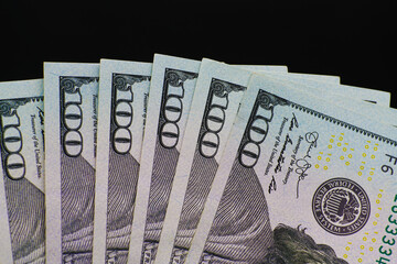 US 100 dollar notes fanned out on black background.