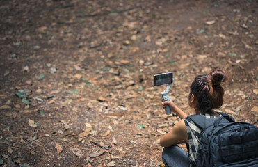 Young women backpacker sitting on ground and using smart phone with gimbal , camping activity , freedom and inspiration concept