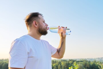 Middle-aged bearded man drinks water from bottle on hot summer day