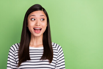 Fototapeta premium Photo of impressed brunette millennial lady look empty space wear striped shirt isolated on green color background