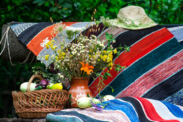 Summer still life with a basket of vegetables, a hat and a decorative carpet