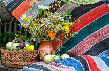 Summer still life with wildflowers and a basket of vegetables. Zucchini in a basket on the background of a decorative carpet