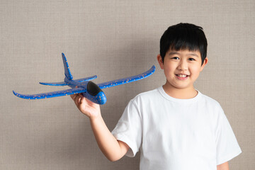 A happy and handsome Asian boy in the white t-shirt is playing his foam plane. A smiling kid is holding an airplane toy. Starting and freedom learning  for children concept.