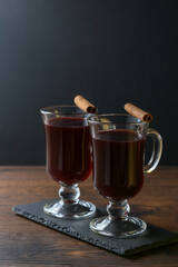 Mulled wine in glass cups with cinnamon and oranges on a wooden table.