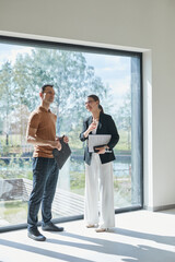Full length portrait of female real estate agent giving apartment tour to young man while standing...