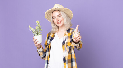 young pretty albino woman smiling proudly and confidently making number one and holding a...