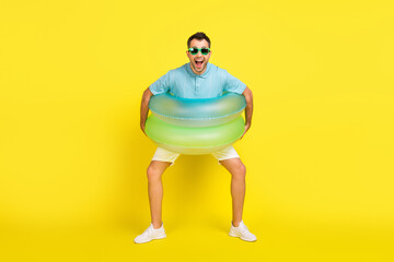 Photo of funny excited young man wear blue t-shirt dark glasses standing inside water circles smiling isolated yellow color background