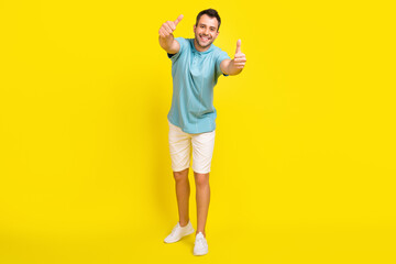 Fototapeta na wymiar Photo of funky attractive young guy dressed blue t-shirt smiling showing thumbs up isolated yellow color background