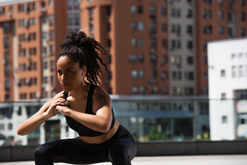 African american sportswoman training in wireless earphone on urban street