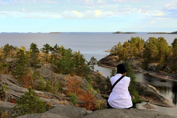 a girl in a white shirt and black panama sits admiring the views of the skerries, the rocky islands of Lake Ladoga