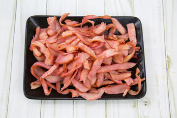 Squid (Lat. Teuthida) half-rings cut into strips on a black rectangular plate with a wooden table background. Food is a delicacy snack for beer.