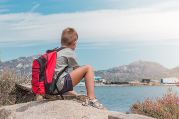 a boy with a backpack looks into the distance at a port at sea
