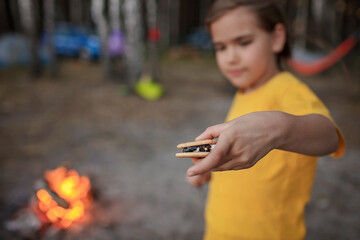 Cute girl roasting marshmallow to make smores over fire flame during camping, traditional American food, active recreation and family travel