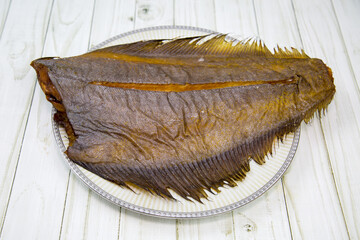 Cold smoked halibut without a head is appetizing on a round plate with a wooden table background....