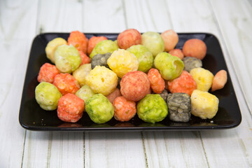 Bright cheese balls mix on a black rectangular plate with a wooden table background. Food is a delicacy snack for beer.