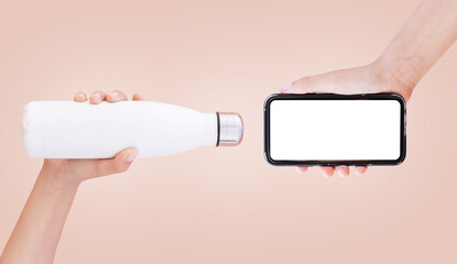 Close-up of white bottle and smartphone with mockup in hands, on light brown.