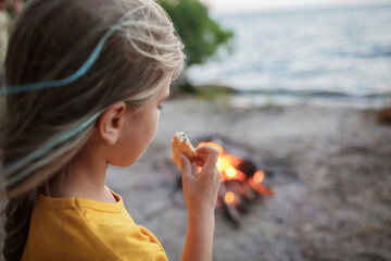 Cute girl roasting marshmallow to make smores over fire flame during camping, traditional American food, active recreation and family travel