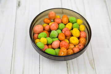 Peanuts in a glaze mix of bright multicolored flowers on a black round plate with a wooden table...