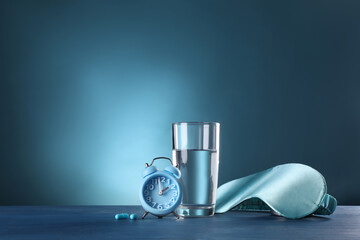 Alarm clock, soporific pills, sleeping mask and glass of water on blue wooden table, space for text. Insomnia treatment