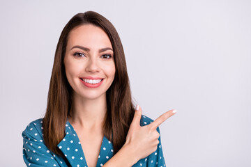 Photo of sweet shiny young lady wear dotted shirt pointing finger empty space smiling isolated grey color background